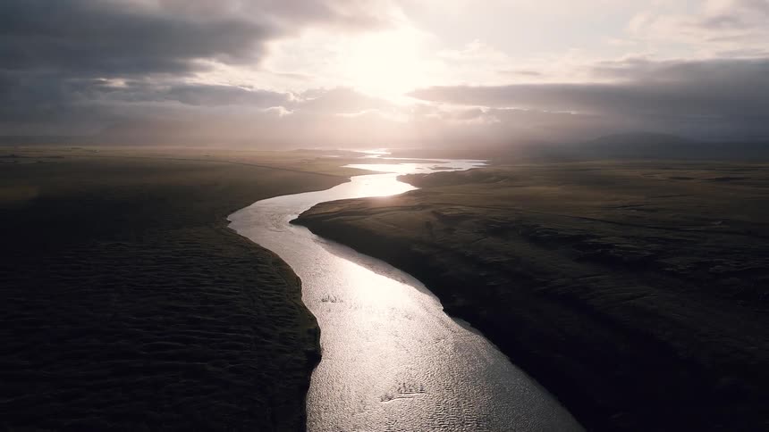 Meandering river reflecting the sunlight at dusk over a vast plain