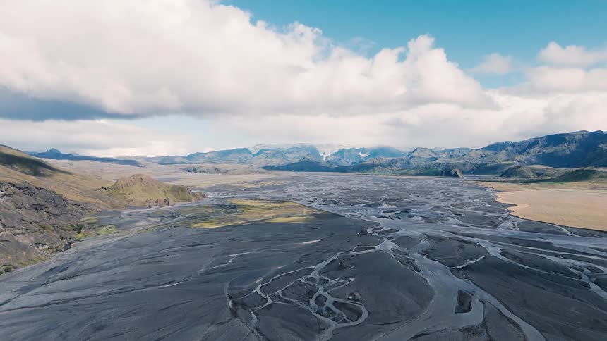 Winding channels over dark terrain surrounded by mountains under a blue sky