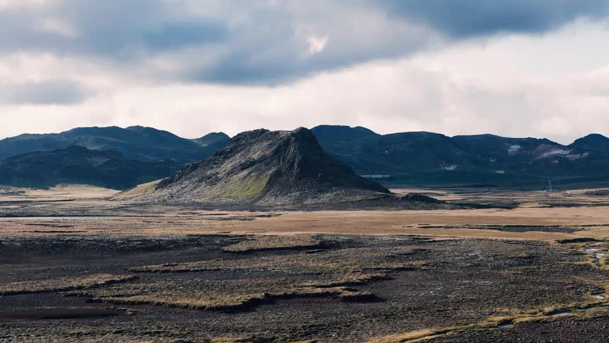 A vast valley landscape stretches wide with a mountain range in the background at midday