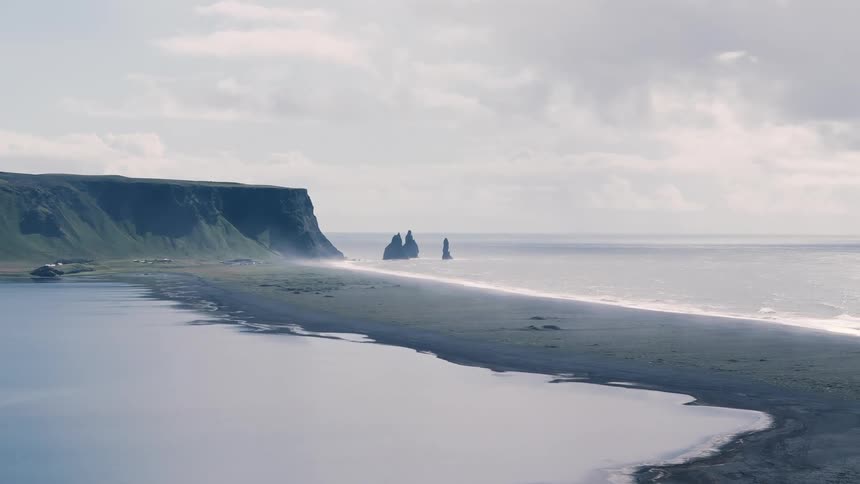 Beach next to the ocean with unique landforms in the background outdoors