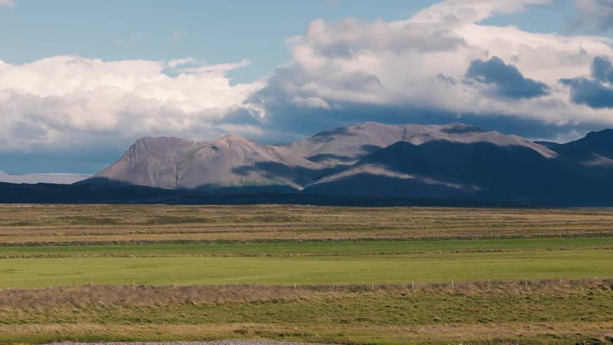 Vast green fields with mountains in the background under a partly cloudy sky