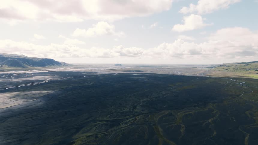 Vast landscape with dark terrain and winding veins under a partly cloudy sky