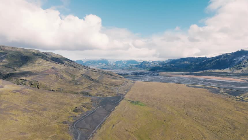 Wide plain with braided rivers surrounded by mountains under a blue sky