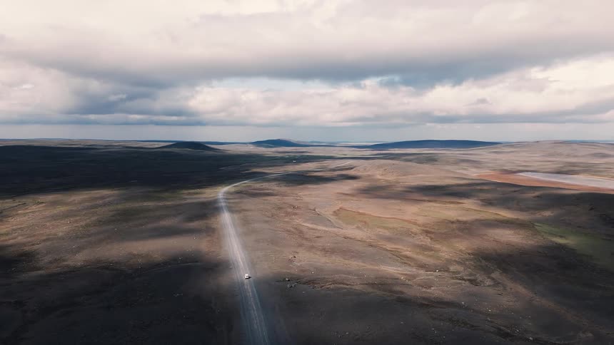 Straight road cutting through a vast arid landscape under a cloudy sky