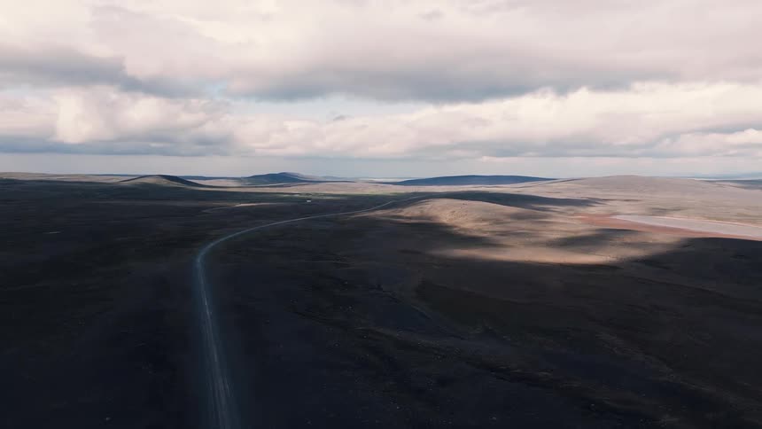 Person walks along winding road in barren landscape under dramatic sky with clouds and diffused light