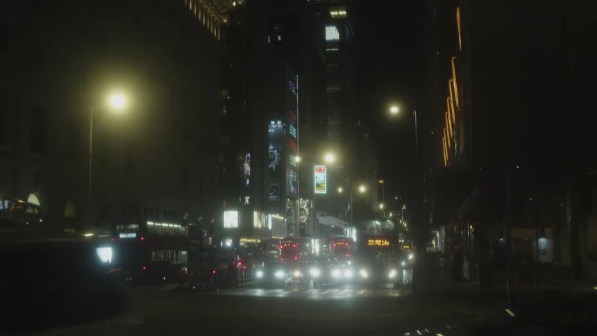 A series of cars and buses move through an intersection while other vehicles stop in traffic on a busy city road at night