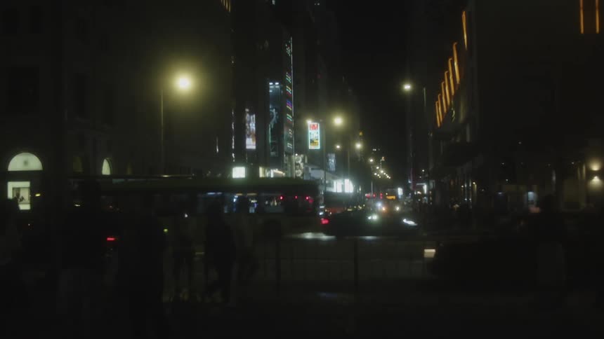Pedestrians and heavy vehicular traffic move through a downtown intersection at night