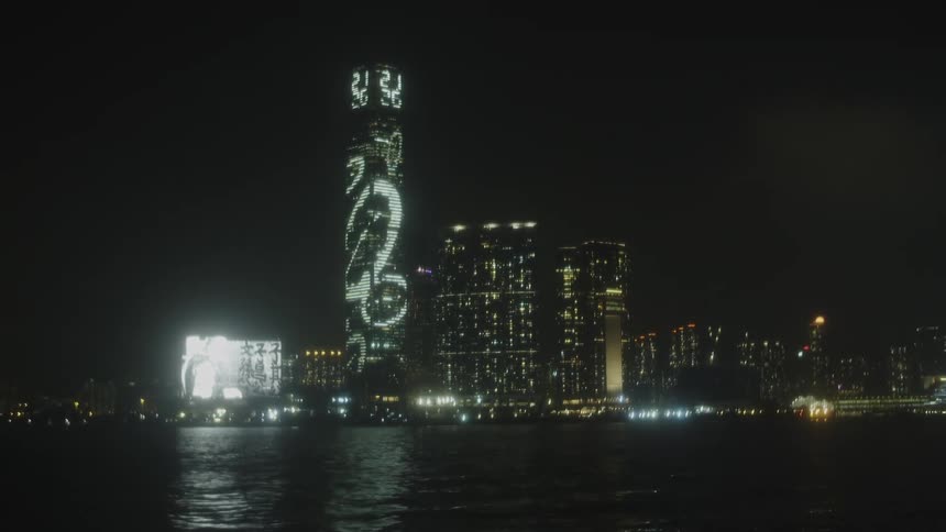 A city on the shoreline at night with numerous highrise buildings and skyscrapers illuminated by lights along the waterfront