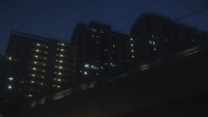 Multiple tall residential structures silhouetted against a dark sky and a train passing by