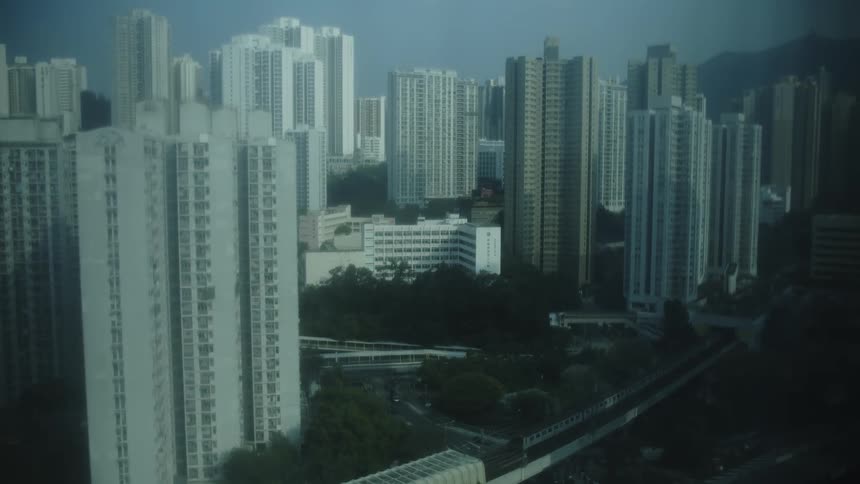 Elevated view of an area featuring a large concentration of residential towers set against a pale sky with lowrise structures and transportation infrastructure visible below