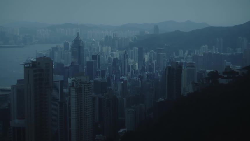 Urban skyline at dusk with skyscrapers surrounded by mountains and water in the background