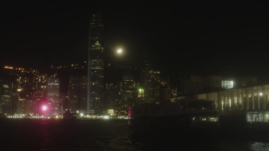 A city skyline glows at night from the shoreline with lights illuminating the highrise buildings and skyscrapers