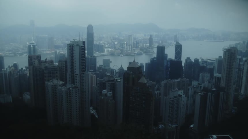 Highangle view of a vast collection of tightly packed tall structures extending towards a body of water with hazy mountains in the distant background