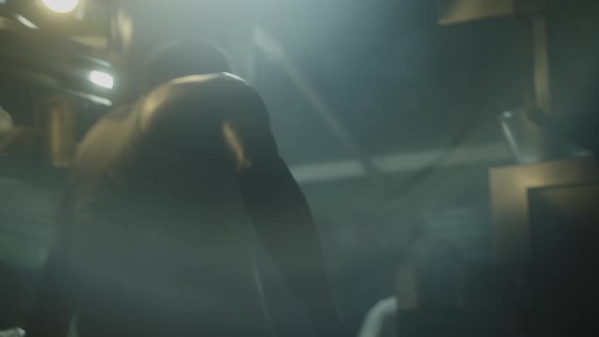 An asian man with his back to the camera working over a lidded cooking vessel with a bright light source behind the figure creating a silhouette and illuminating rising vapor