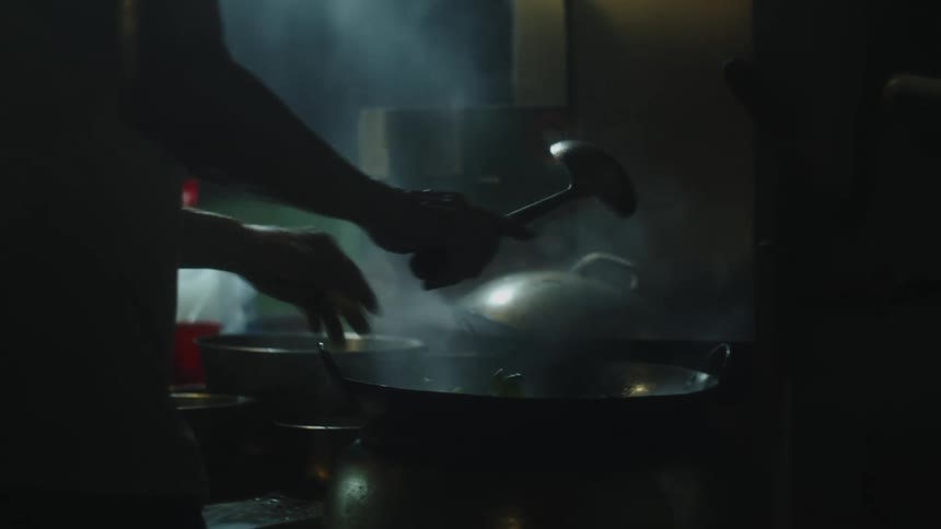 Person lifting lid off large pot with rising steam in dimly lit kitchen