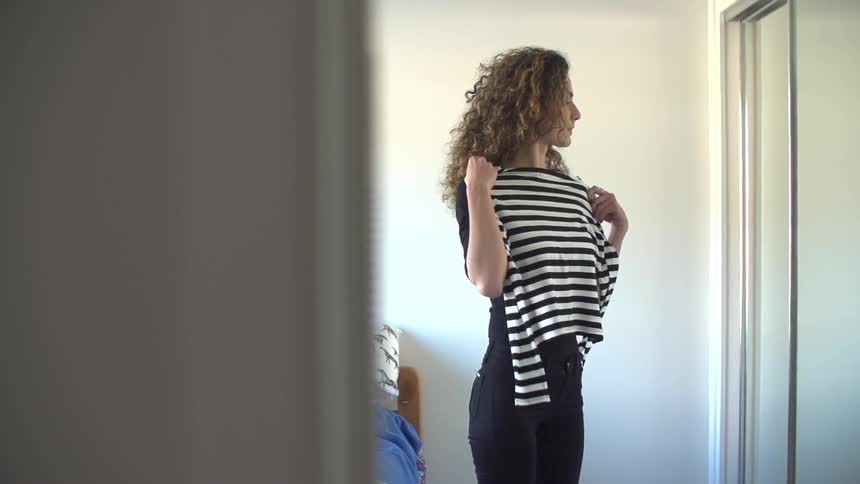 Woman holding a shirt up to her chest while looking in the mirror