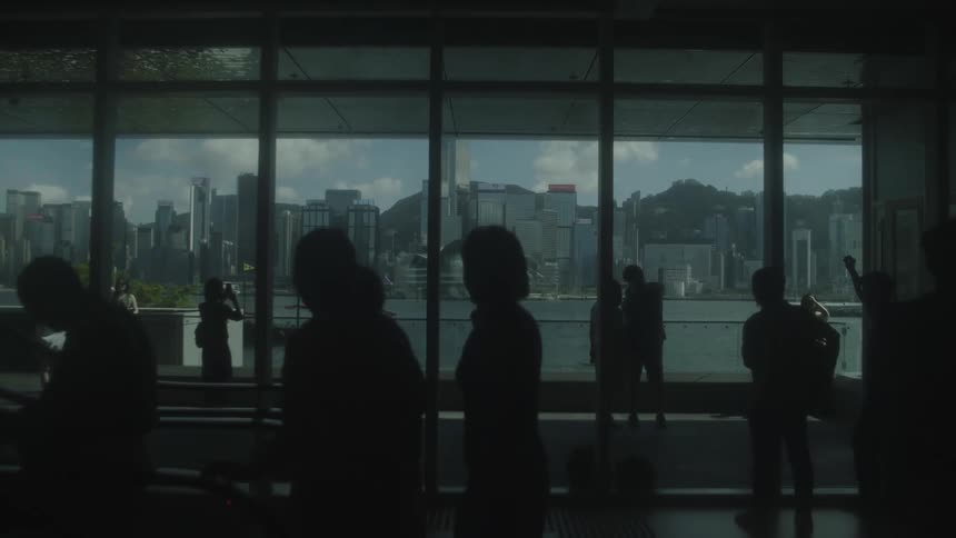 Silhouettes of people near large windows reveal the urban view in the background