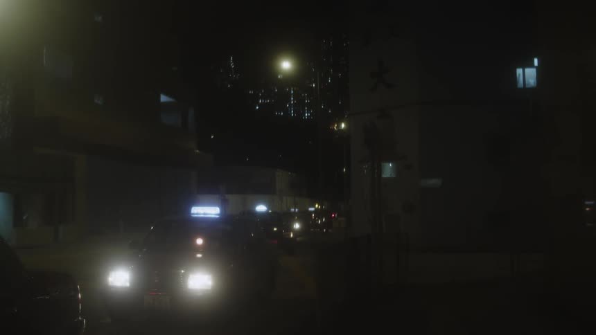 Two taxicabs park at the side of a city street at night