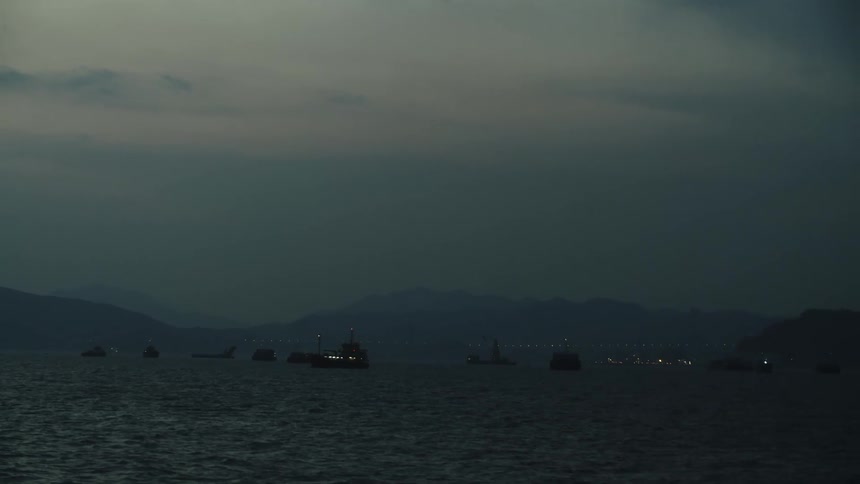 Illuminated vessels sail on dark waters under a cloudy sky at dusk