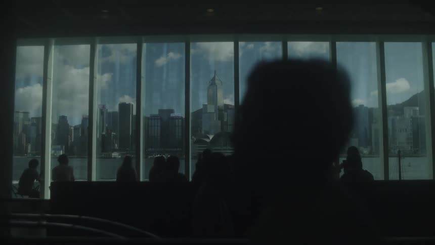 Silhouettes of people observe the urban skyline through large glass windows