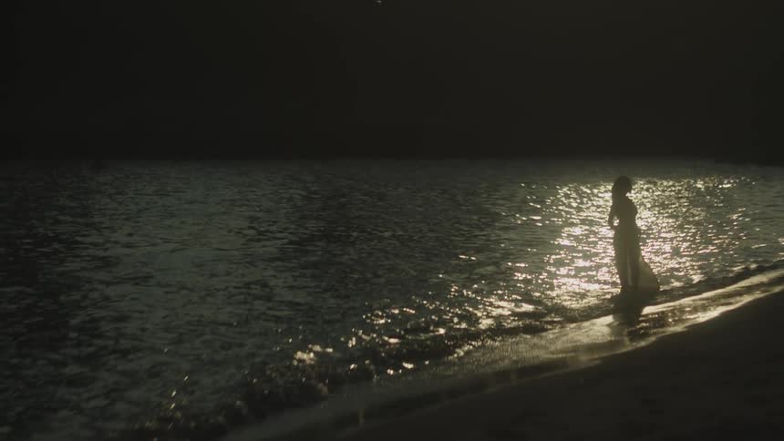 Female silhouette stands by the sea under the soft light reflected on the water at dusk
