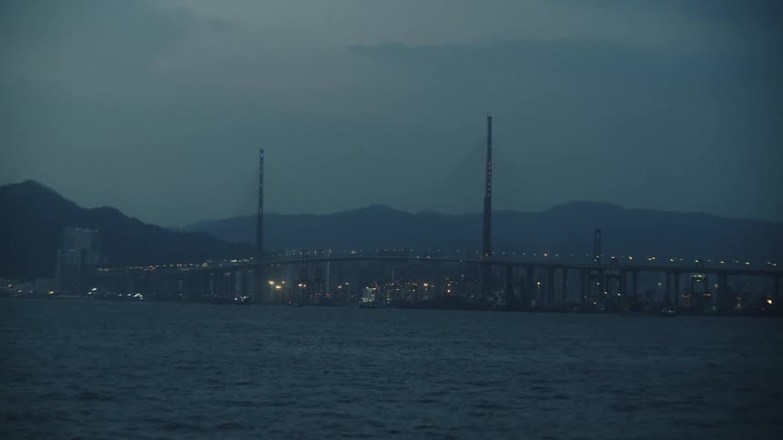 A cityscape with a long bridge stretching across water at dusk