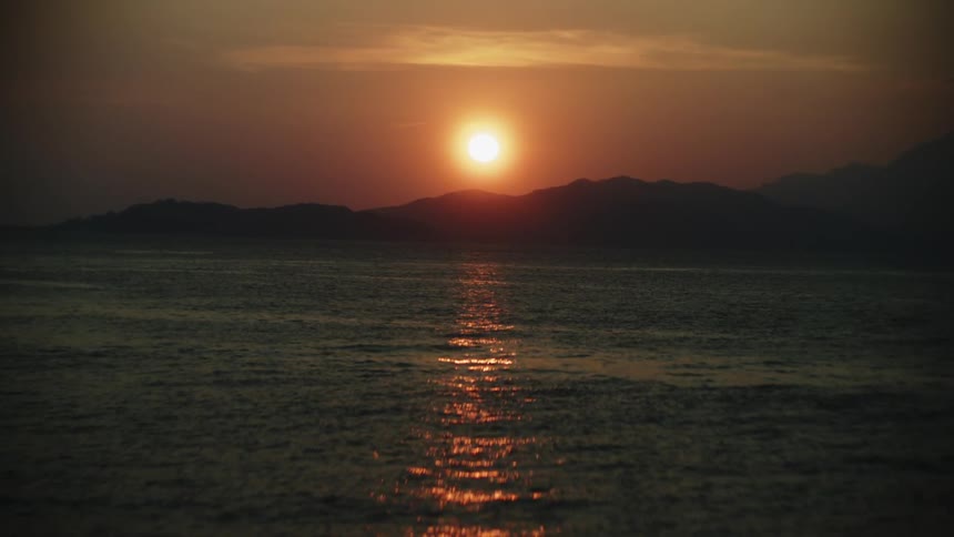 Sun sets behind the mountains reflecting orange tones across the surface of the sea