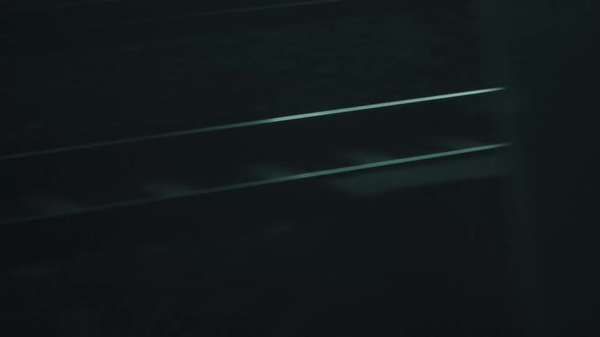 The sleek dark surface of train tracks with light reflecting off the rails in a moody atmospheric setting