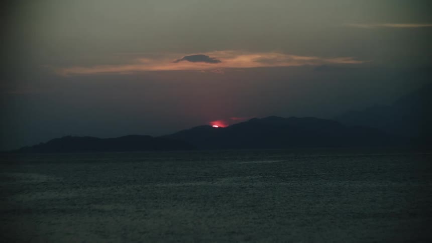 Dark mountain silhouettes with the sun above a calm ocean