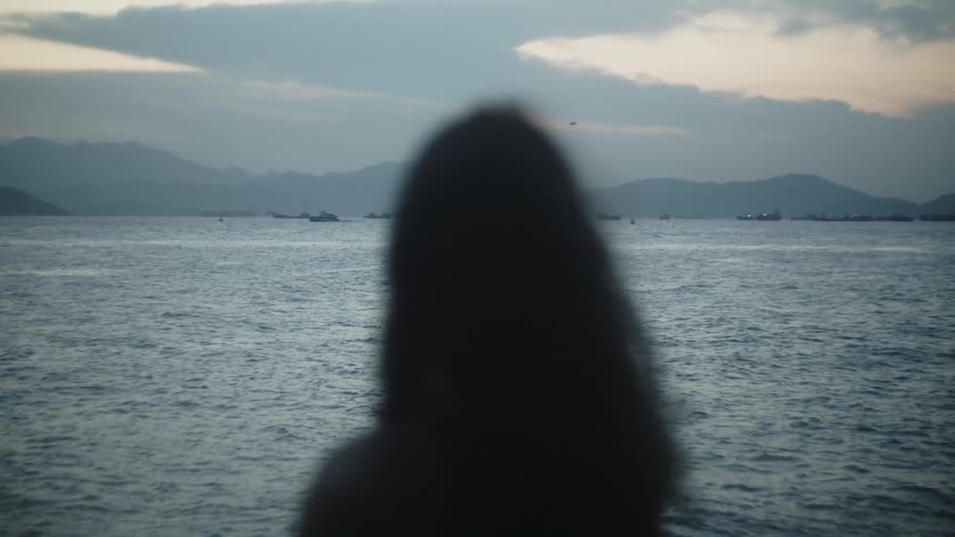 Person overlooks the ocean with boats and distant mountains at sunset