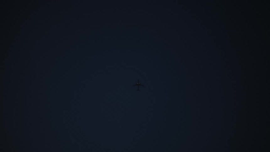 An airplane flies across a dark sky at night