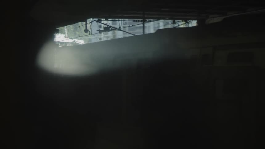 A passenger train pulls away from a darkened station on a summer day