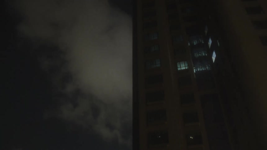 A city skyscraper rises into the night its windows glowing with light as dark clouds drift across the sky above