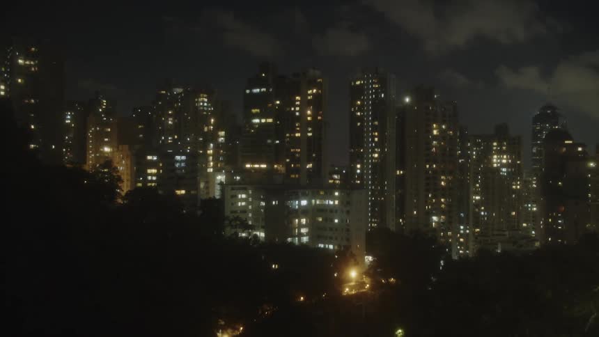 City skyline on a hill at night with lit skyscrapers framed by dark foliage