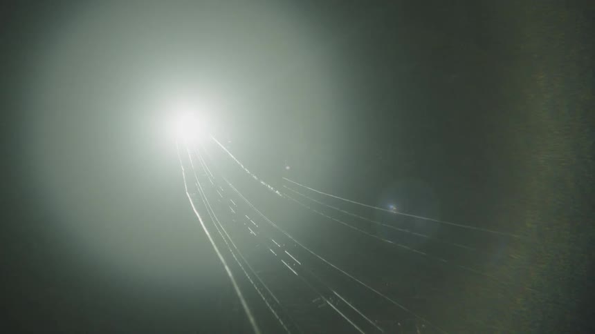Train tracks vanish into the darkness as a bright light appears in the distance