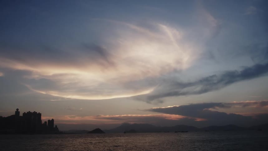 A city skyline by the calm ocean under a dramatic coastal sunset