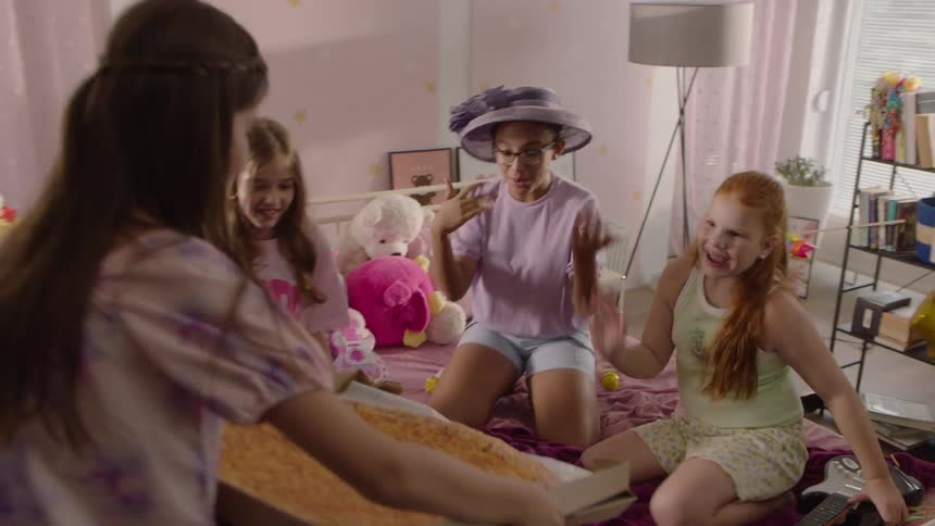 A group of young girls have a party at midday and excitement fills the bedroom as one of them brings in a pizza