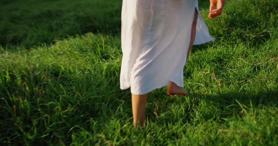 The woman walks barefoot through the grass
