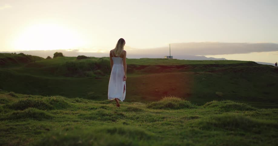 The woman walks on the grassy hills towards the shore