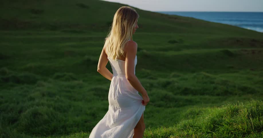 Woman smiles while looking back as she walks through a green field near the sea