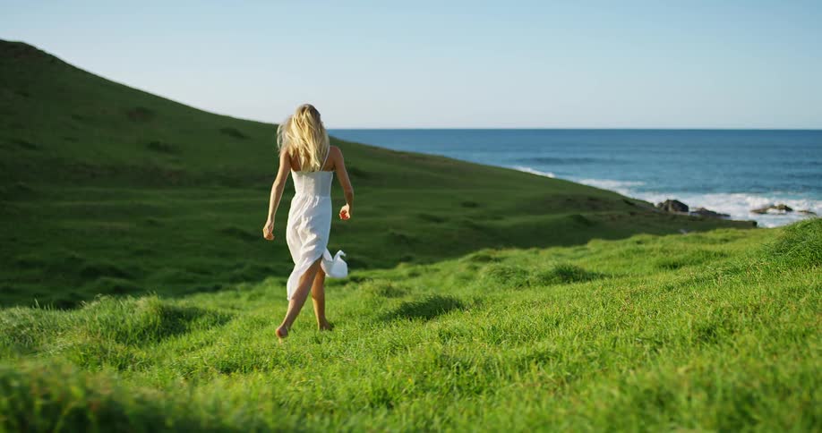 A young woman running through a grass field next to the ocean coast during daytime