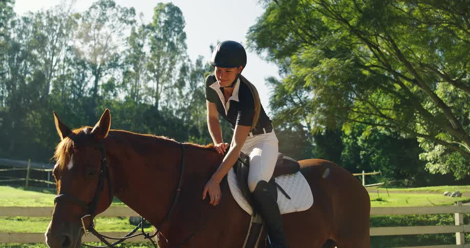 Rider wearing a helmet pets her horse during a ride in a green area