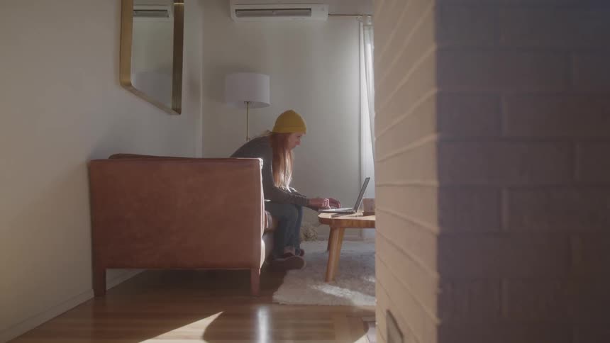 Woman sitting in the living room during the daytime types on a laptop