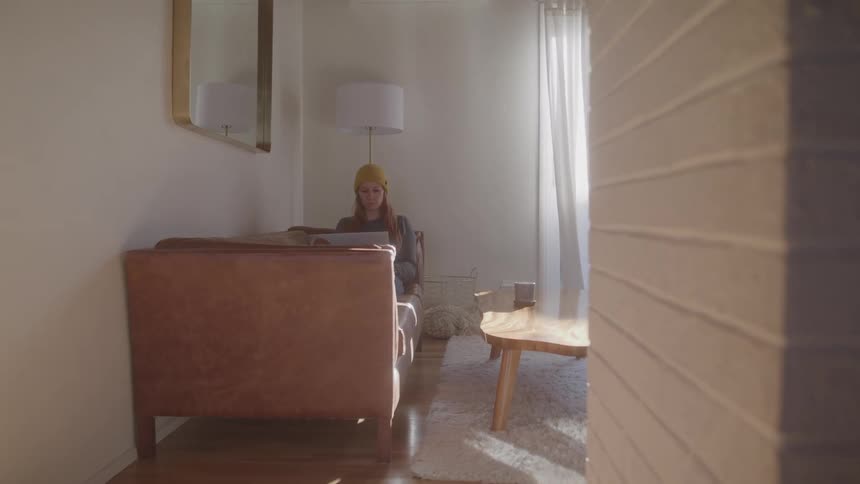 A young woman using a laptop computer while sitting on a couch in a living room during daytime
