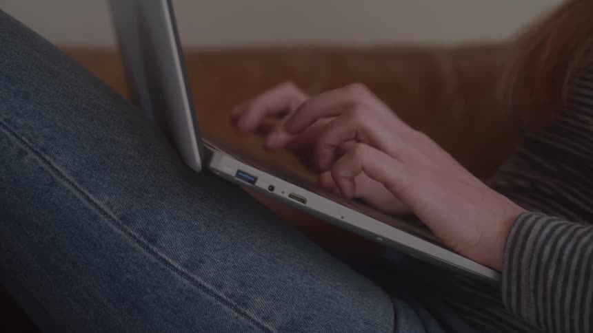 A woman with red hair is typing on a laptop sitting in a couch in an indoor setting