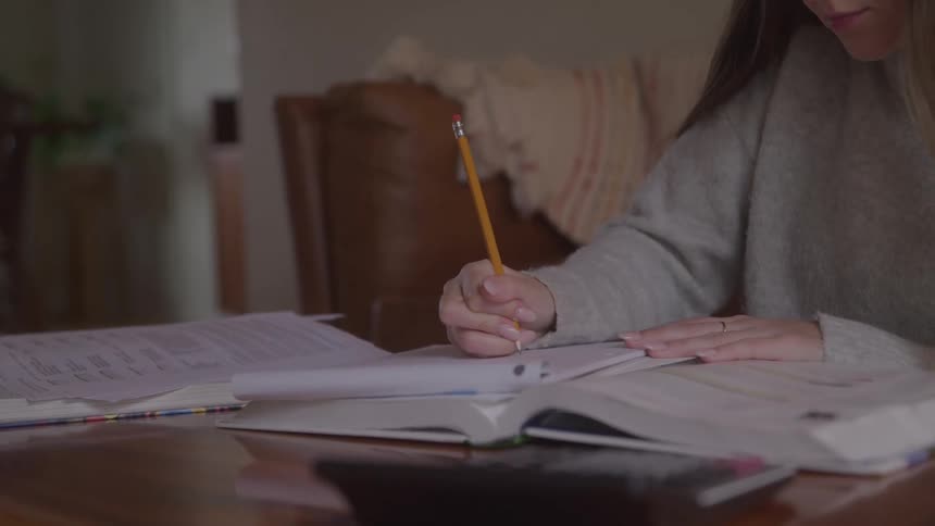 A female sits at a table writing on paper using a pencil