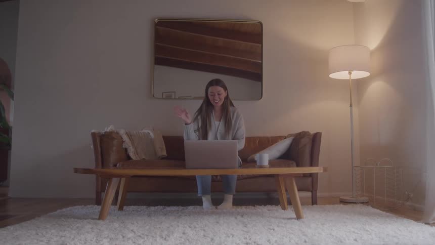The woman smiles and waves at her laptop