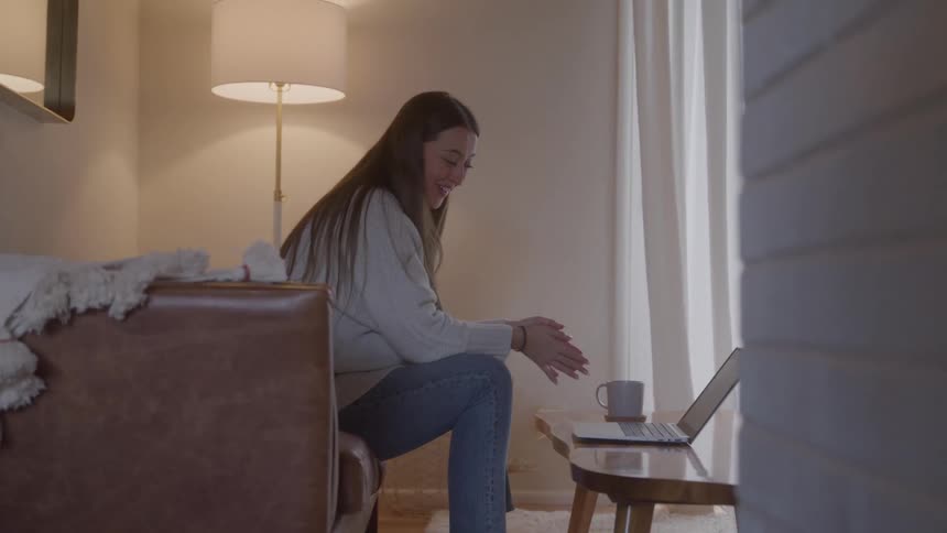 Woman sits on a couch laughing during a video call indoors