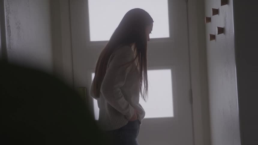The woman is standing by her door inside