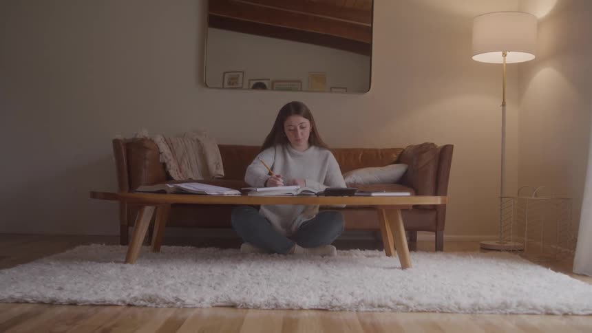 Woman sits on the floor studying in a cozy indoor living room